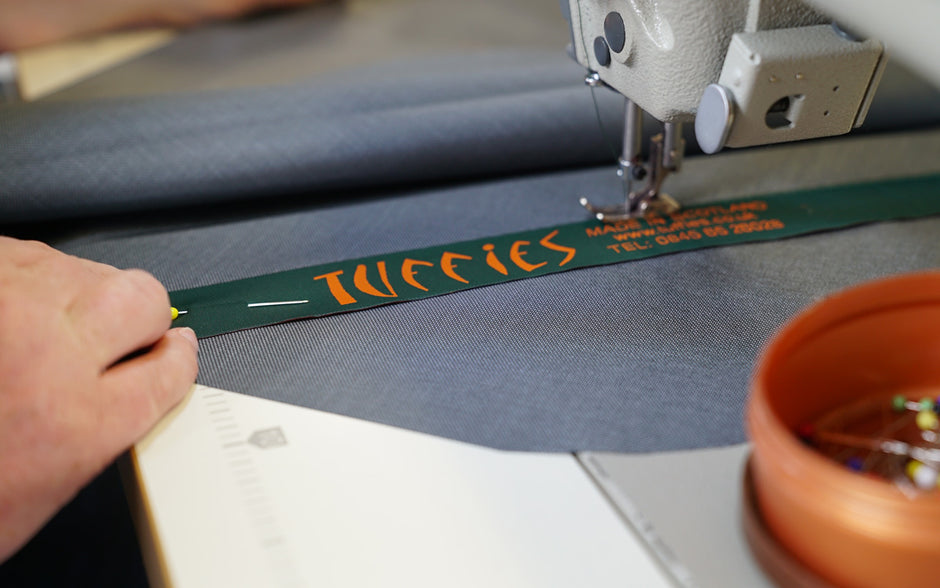 Person sewing a label with 'Tuffies' branding onto a Tuffies dog bed using a sewing machine.